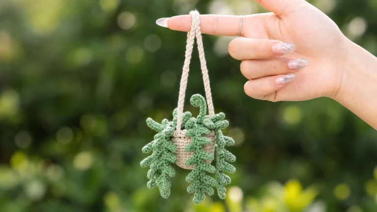 Easy crochet projects example — a mini crochet hanging fern plant in a beige pot dangling from a cord outdoors.