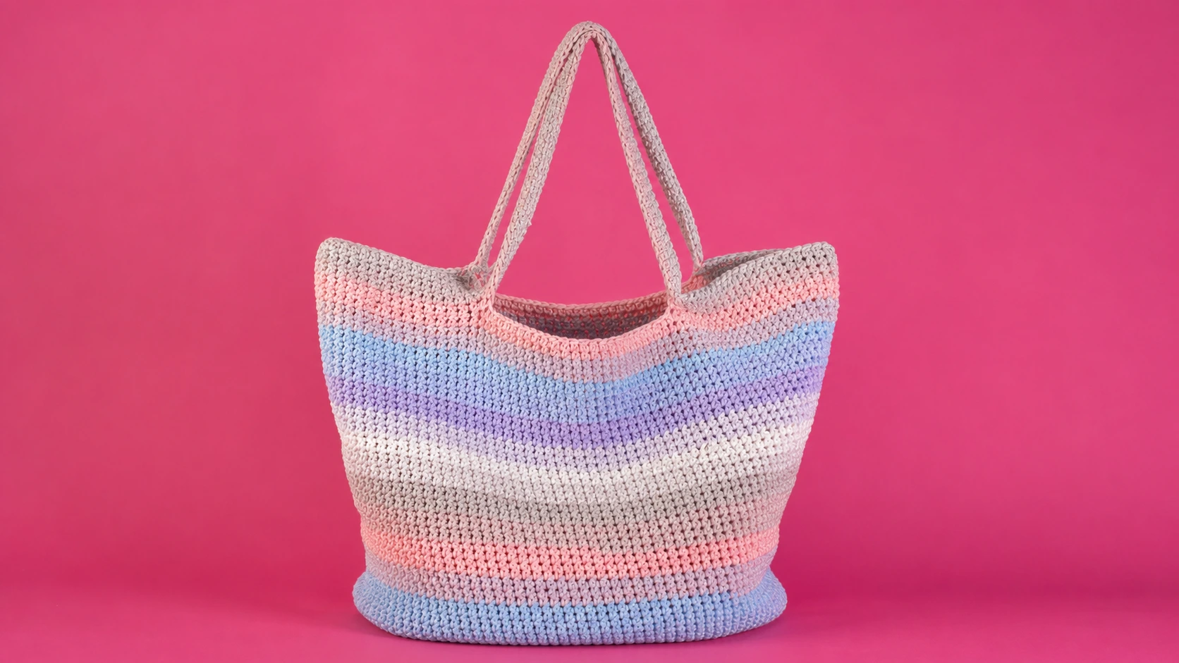 Free crochet patterns example — a pastel striped crochet basket tote bag with two long handles on a pink background.